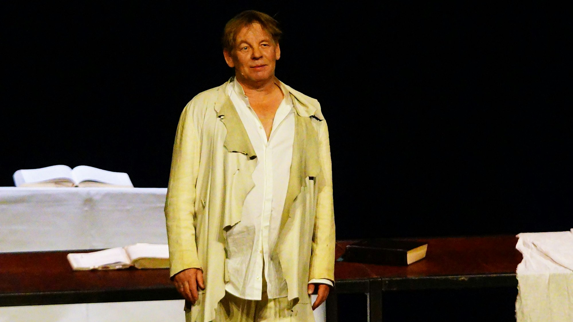 Ein Mann steht in heller, weiter Kleidung auf einer Bühne.