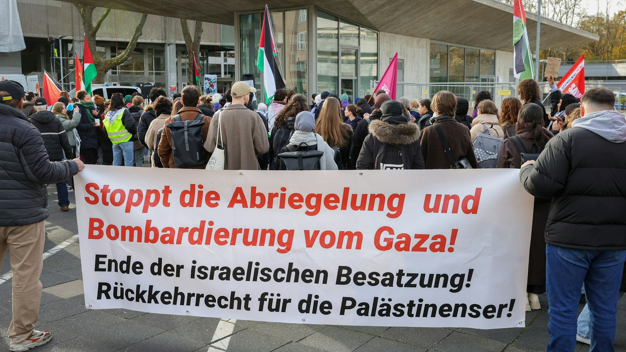 Demonstrierende stehen vor dem Hauptgebäude der Uni Köln mit einem Plakat mit der Aufschrift „Stoppt die Abriegelung und Bombardierung vom Gaza“.