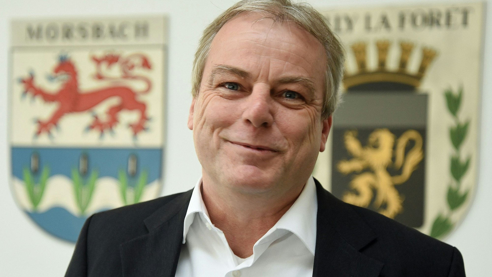 Zum 1. April übernimmt Oliver Moritz die Leitung der Morsbacher Entwicklungsgesellschaft als hauptamtlicher Geschäftsführer. Dort arbeitet er indes schon seit diesem Oktober. Unser Bild zeigt ihm in Ratssaal vor dem Morsbacher Wappen und dem der Partnergemeinde Milly-la-Forêt (rechts).