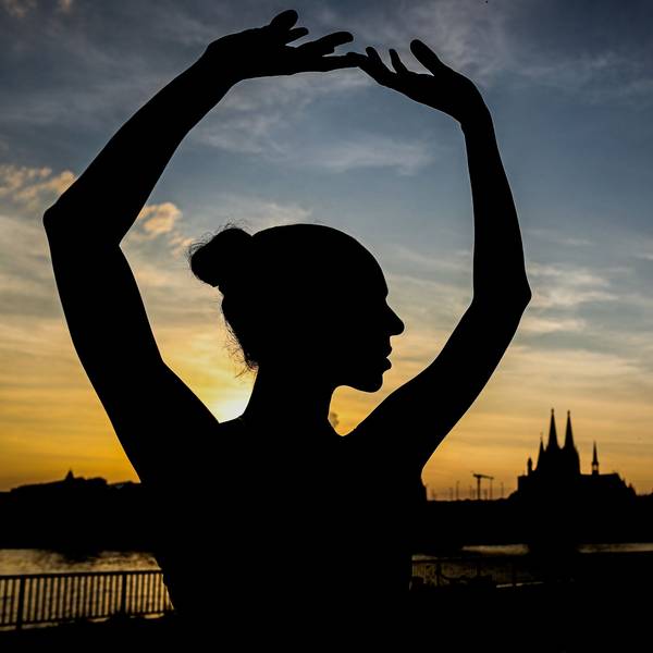 Ein Schatten einer Tänzerin vor blau-goldenen Himmel mit Sonnenuntergang, im Hintergrund die Silhouette des Doms.