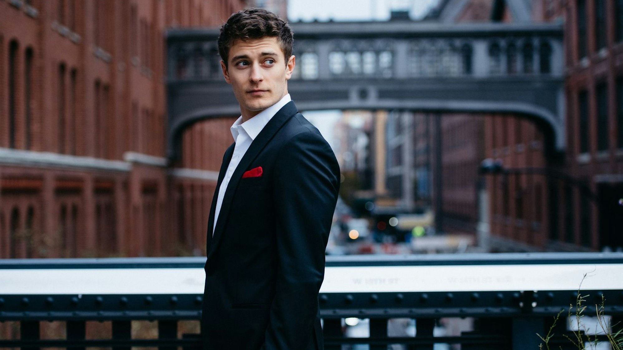 Jakub Józef Orlínski auf einer Brücke, im Hintergrund städtischer Verkehr. Der Sänger trägt einen schwarzen Anzug mit weißem Hemd und einem roten Taschentuch im Revers.