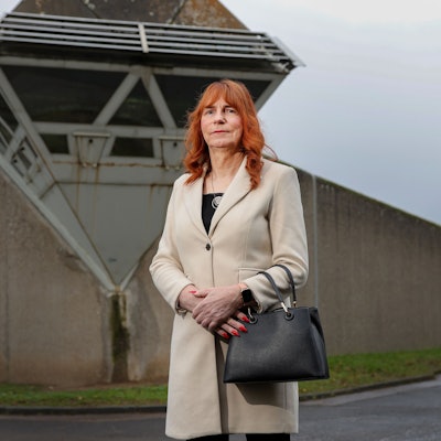 Eine Frau mit rötlichen Haaren steht vor der Mauer des Gefängnisses.