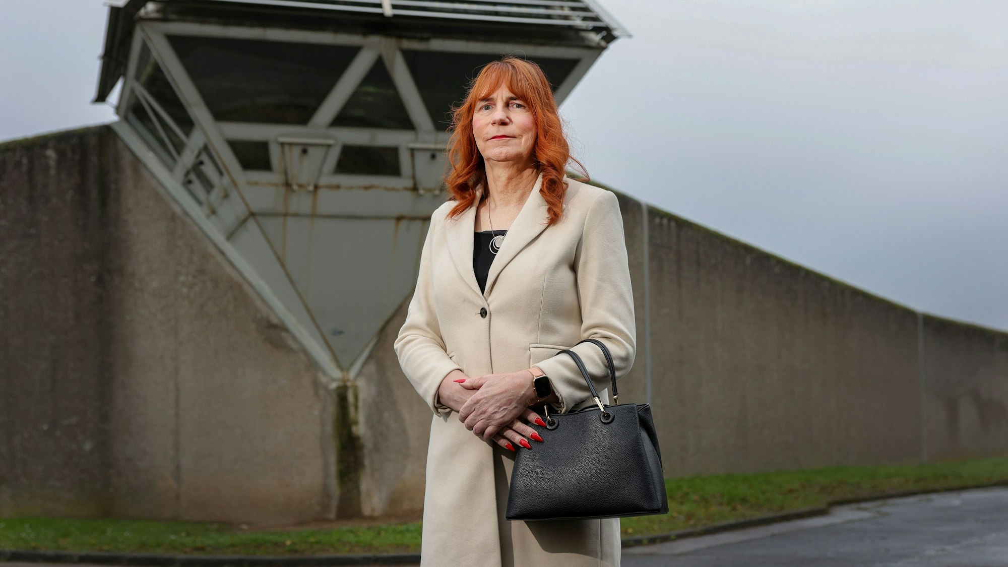 Eine Frau mit rötlichen Haaren steht vor der Mauer des Gefängnisses.