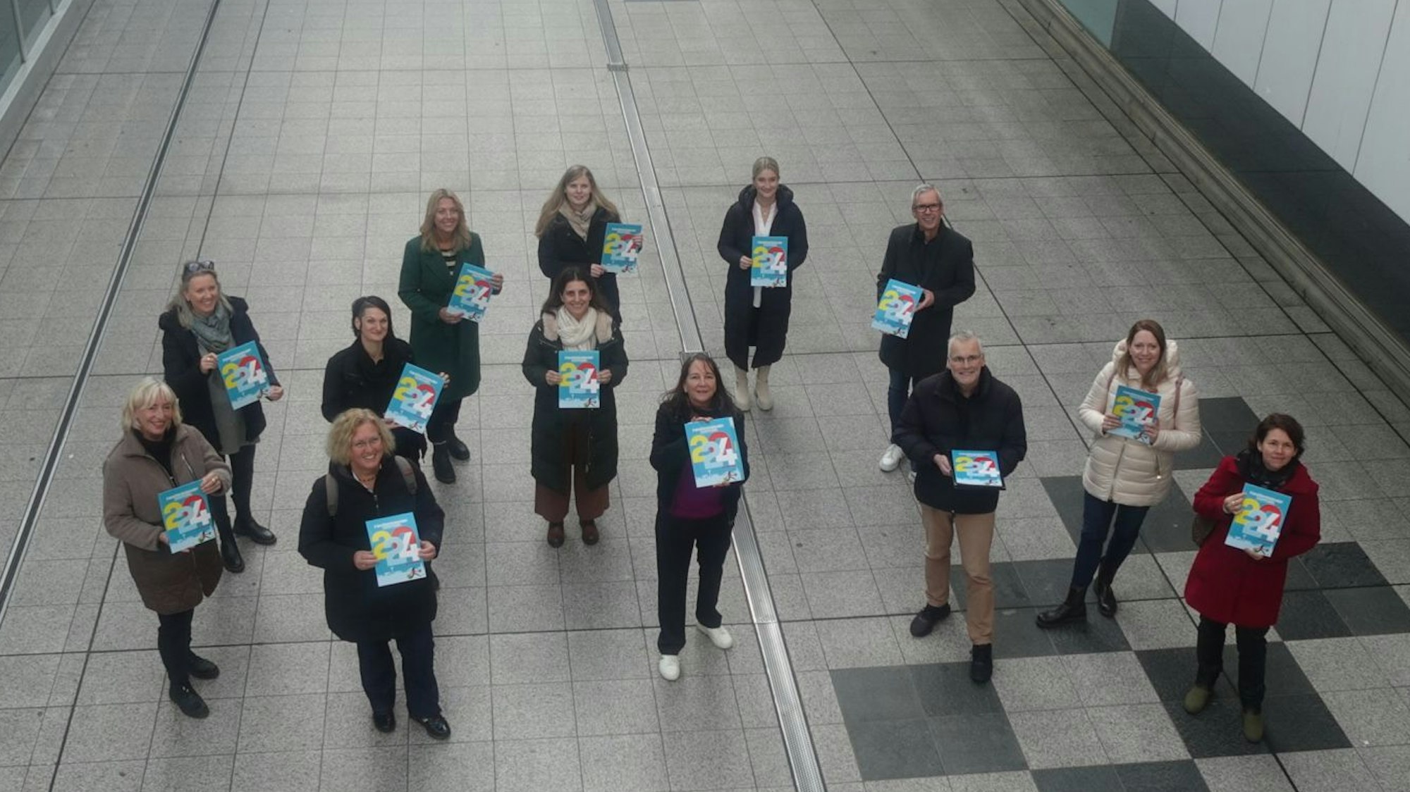 Elf Frauen und zwei Männer stehen in der Fußgängerzone und halten einen Familienkalender in der Hand.