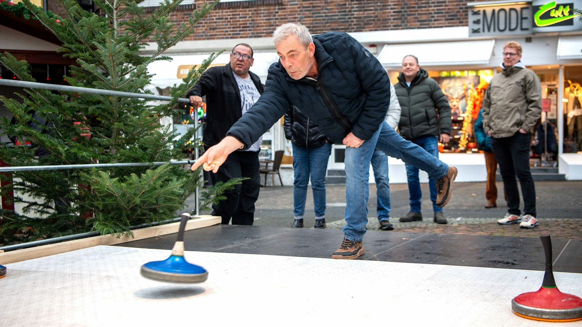 Das Bild zeigt einen Mann, der gerade einen Eisstock auf die Reise schickt. Eine Gruppe schaut ihm dabei zu.