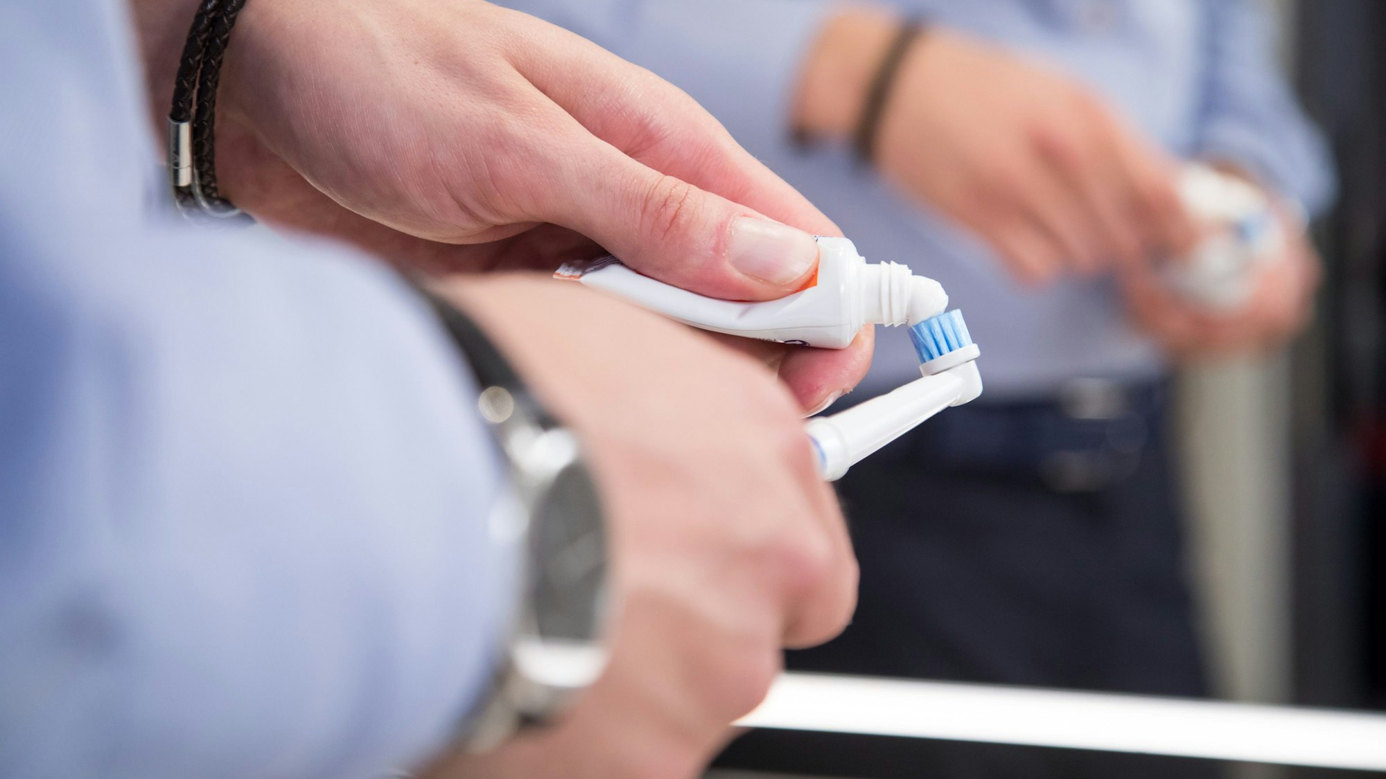 Hände halten Zahnpasta und eine elektrische Zahnbürste.