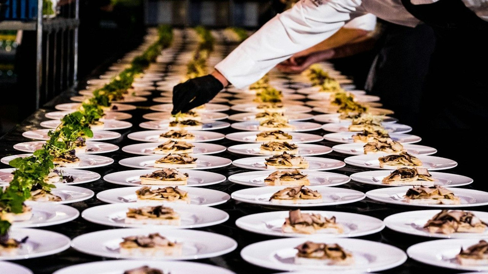 Ein Mitarbeiter eines Catering-Unternehmens richtet Speisen auf einer großen Anzahl von Tellern an.