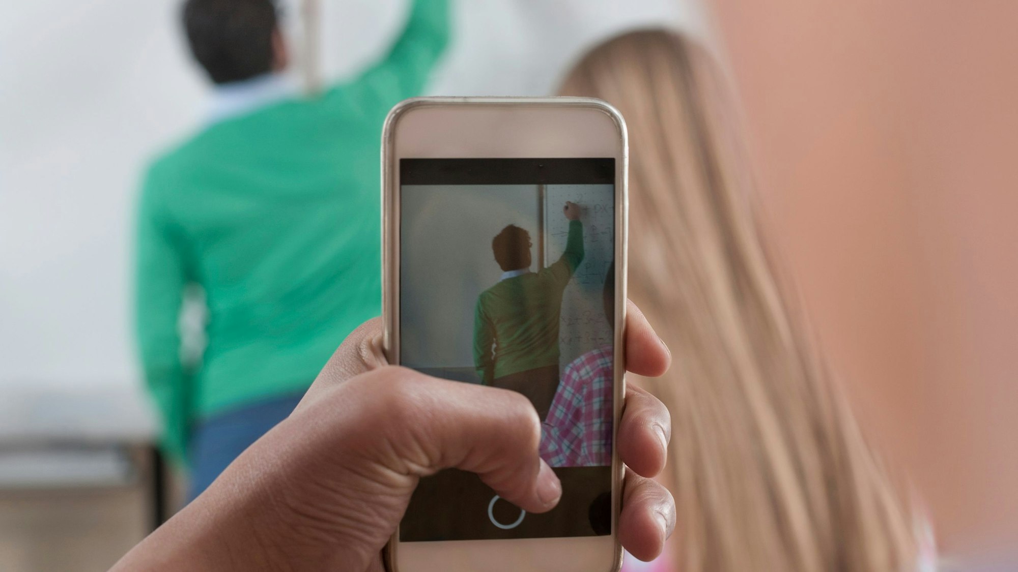 Ein Schüler macht ein Bild vom Lehrer, der etwas an die Tafel schreibt.