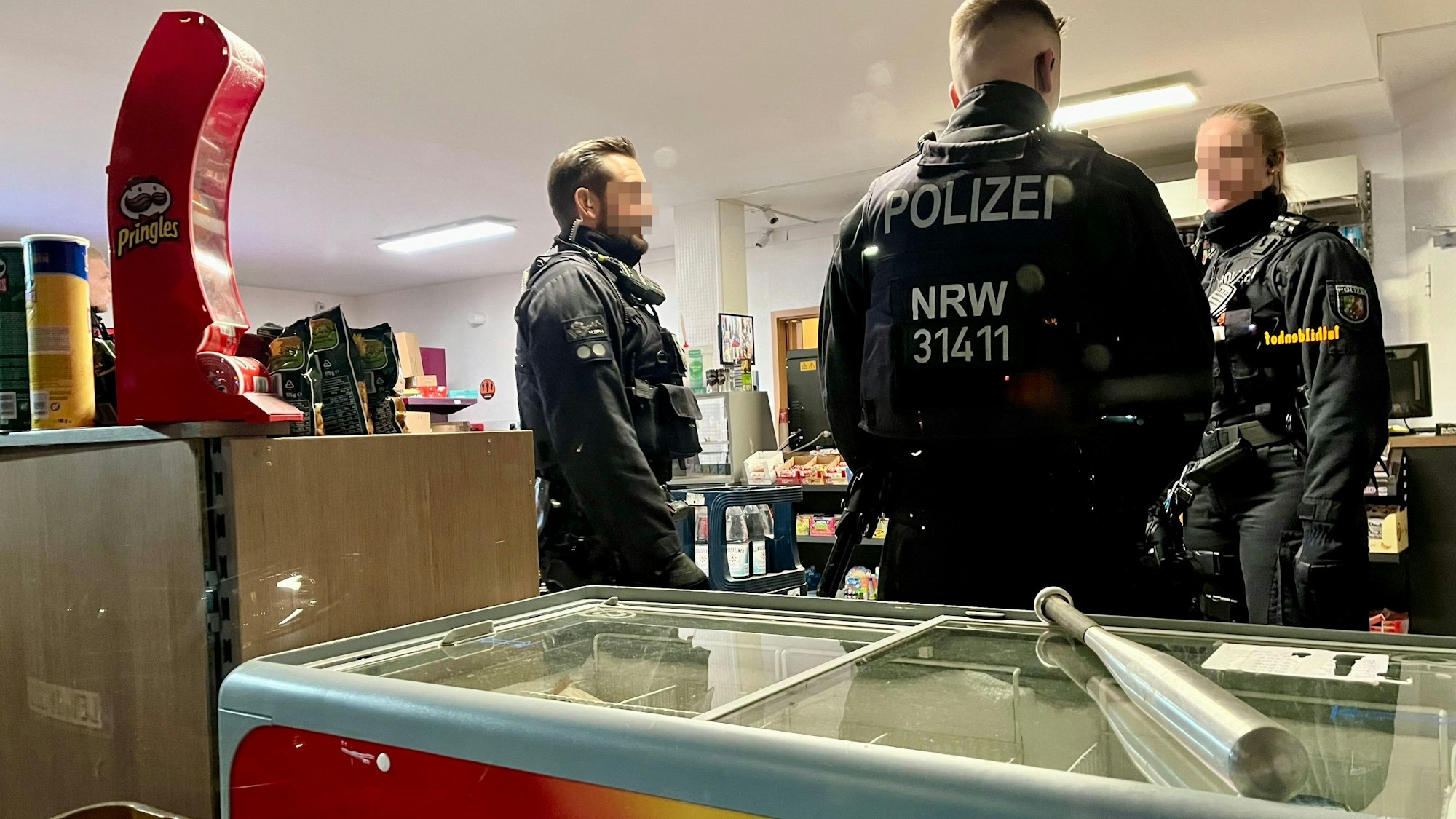 Ein Baseballschläger liegt auf einem Eisschrank, dahinter stehen drei Polizisten.