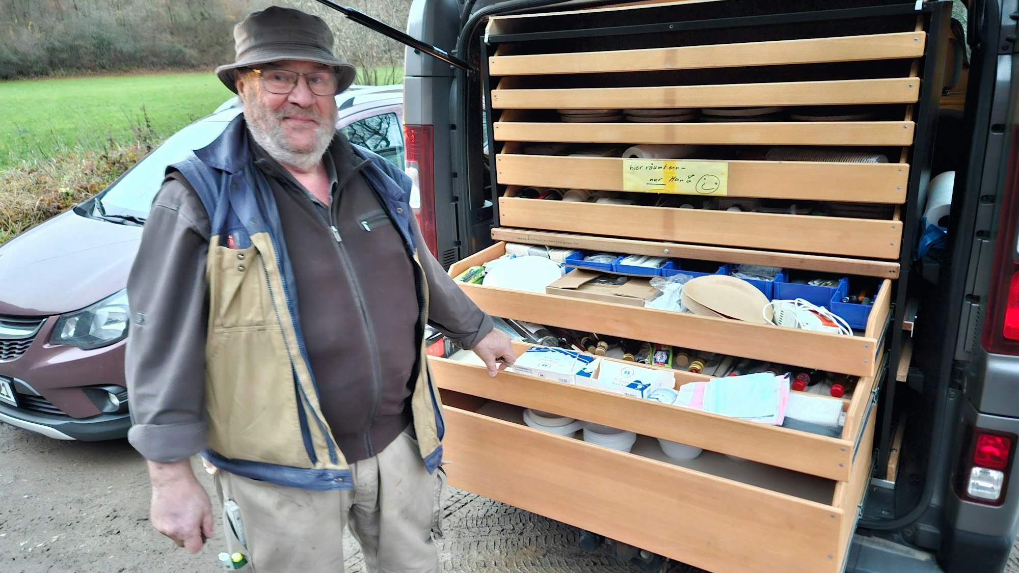 Franz-Heinrich Klinkhammer steht hinter seinem Auto und zeigt auf mehrere ausziehbare Schubladen.
