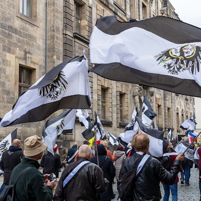 Mehrere hundert Teilnehmer einer Demonstration ziehen mit Flaggen vom Königreich Preußen (schwarz-weiß-schwarz mit Adler) durch die Innenstadt von Dresden (Archivbild). Rund 280 Einsatzkräfte haben am Donnerstag in acht Bundesländern mehrere Objekte im Zusammenhang mit Ermittlungen gegen „Reichsbürger“ durchsucht.