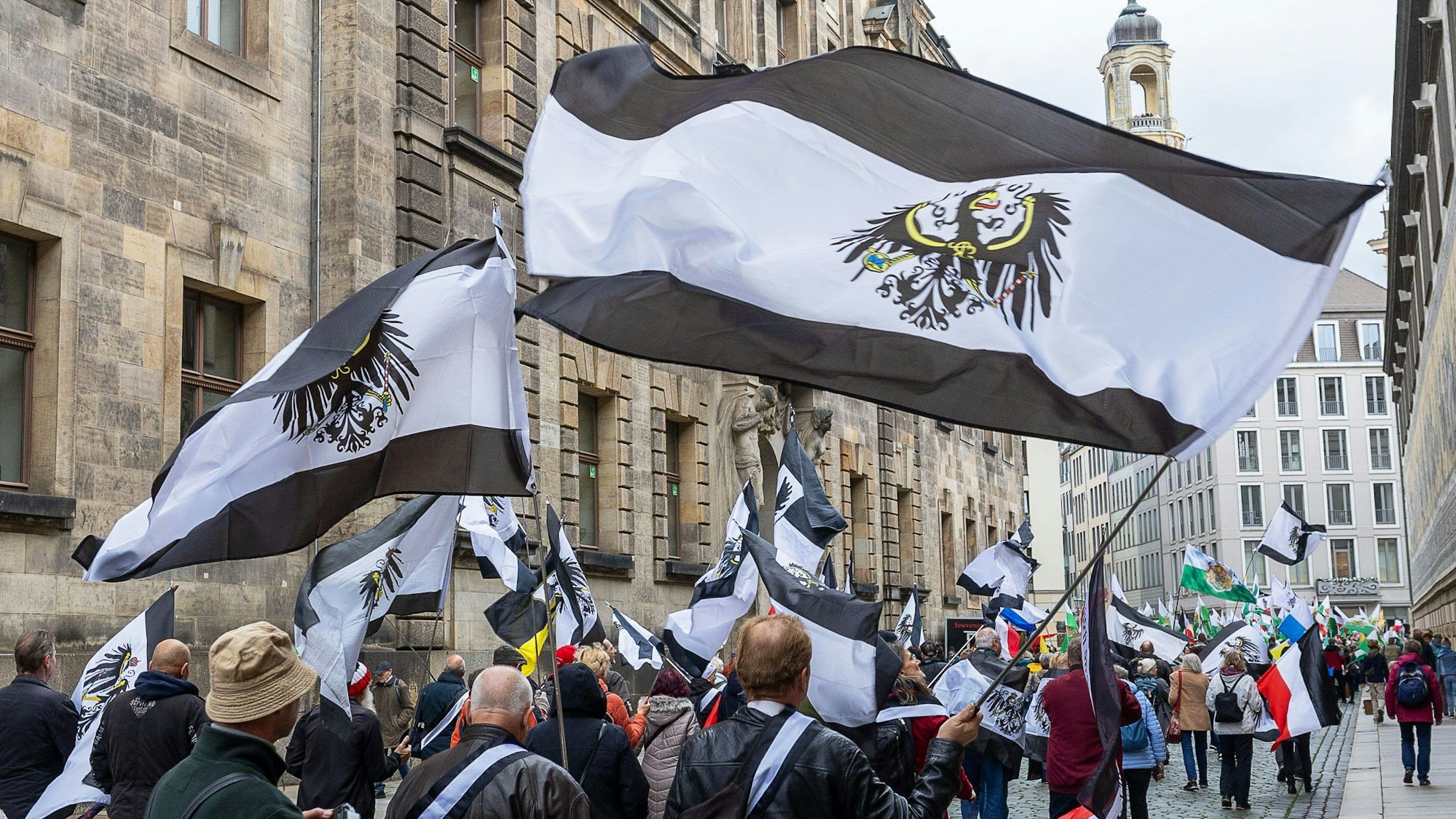 Mehrere hundert Teilnehmer einer Demonstration ziehen mit Flaggen vom Königreich Preußen (schwarz-weiß-schwarz mit Adler) durch die Innenstadt von Dresden (Archivbild). Rund 280 Einsatzkräfte haben am Donnerstag in acht Bundesländern mehrere Objekte im Zusammenhang mit Ermittlungen gegen „Reichsbürger“ durchsucht.