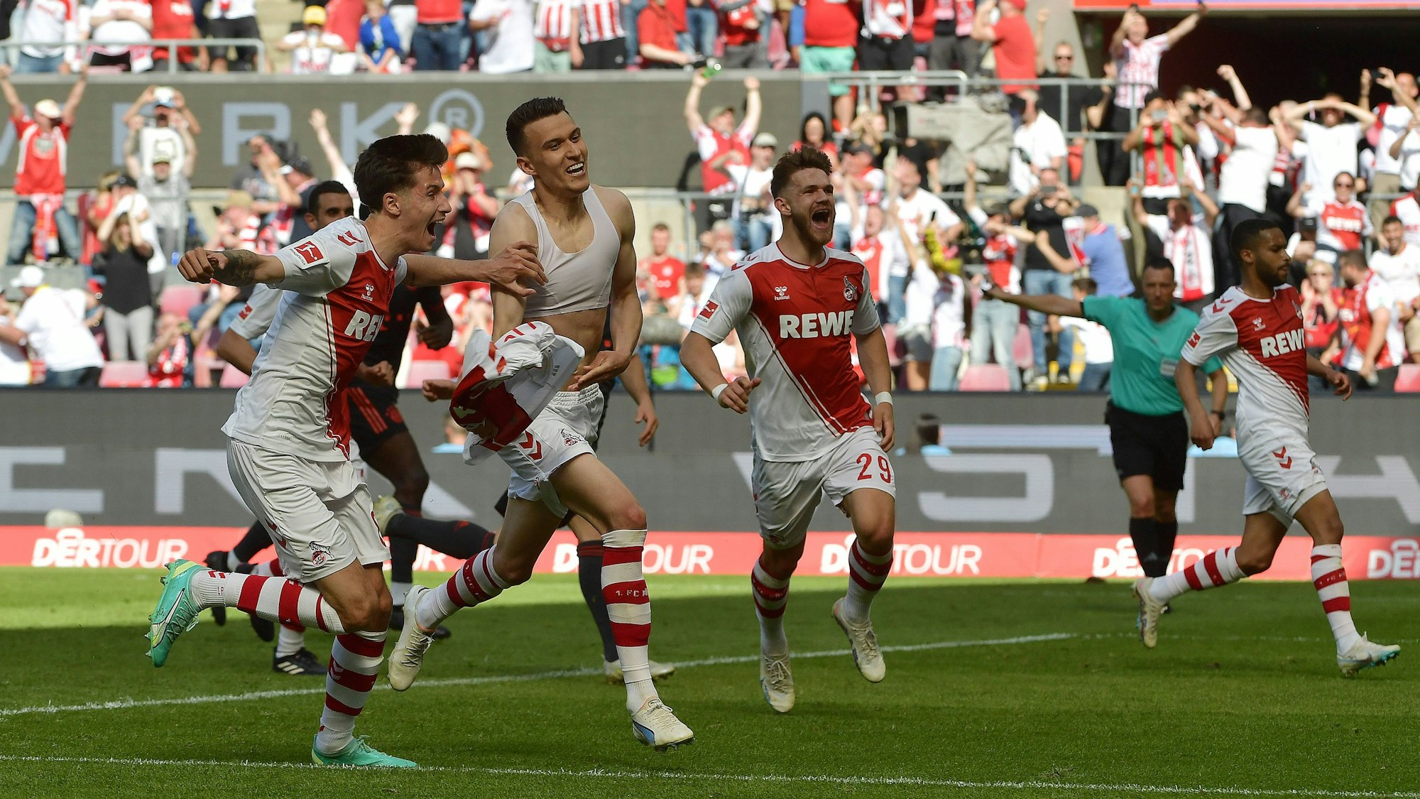 Jubelnd laufen mehrere Spieler des 1. FC Köln über das Spielfeld. Einer hat sich das Trikot ausgezogen.