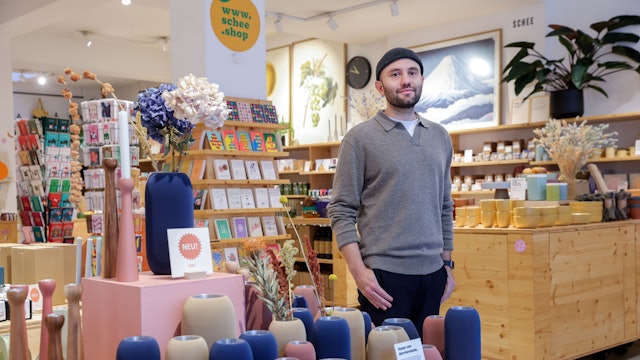 Ein Mann steht in einem Dekoladen mit vielen Vasen und Postkarten.