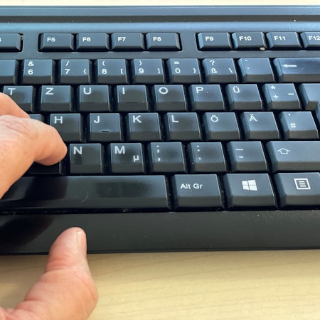 Das Bild zeigt eine Computertastatur und die Finger einer linken Hand.