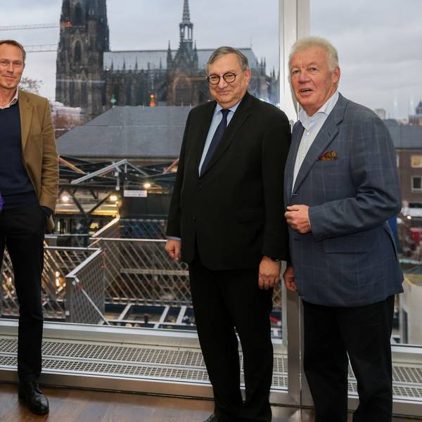 Vier Männer und eine Frau stehen nebeneinander und schauen in die Kamera. Im Hintergrund ist der Kölner Dom zu sehen.