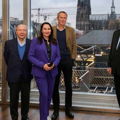 Vier Männer und eine Frau stehen nebeneinander und schauen in die Kamera. Im Hintergrund ist der Kölner Dom zu sehen.