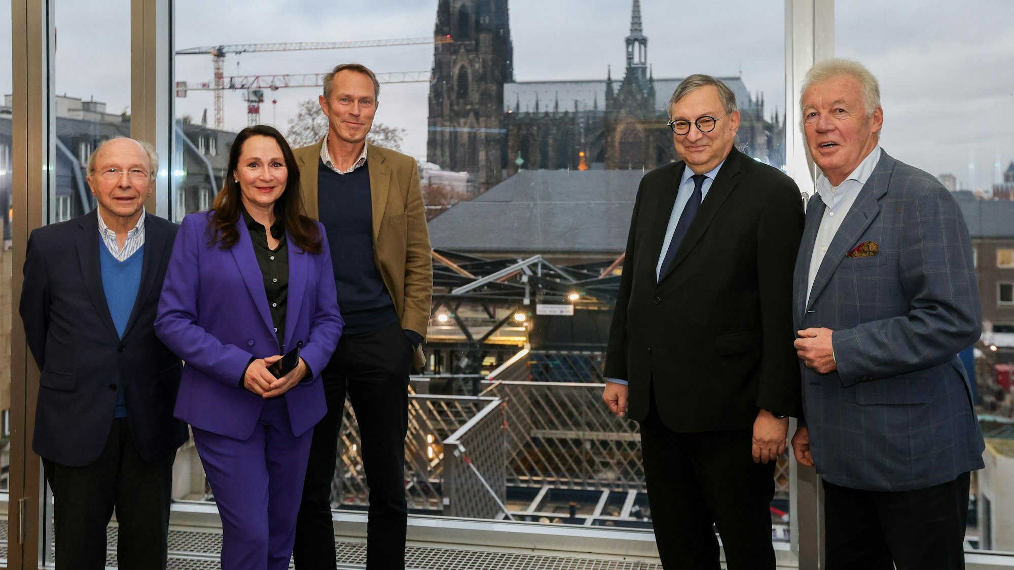 Vier Männer und eine Frau stehen nebeneinander und schauen in die Kamera. Im Hintergrund ist der Kölner Dom zu sehen.