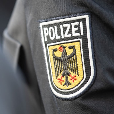 Junge Bundespolizistinnen und Polizisten stehen bei ihrer Vereidigung im Innenhof der Bundespolizeiinspektion am Flughafen Frankfurt, dabei ist ein Polizeiabzeichen auf einem Ärmel zu sehen.