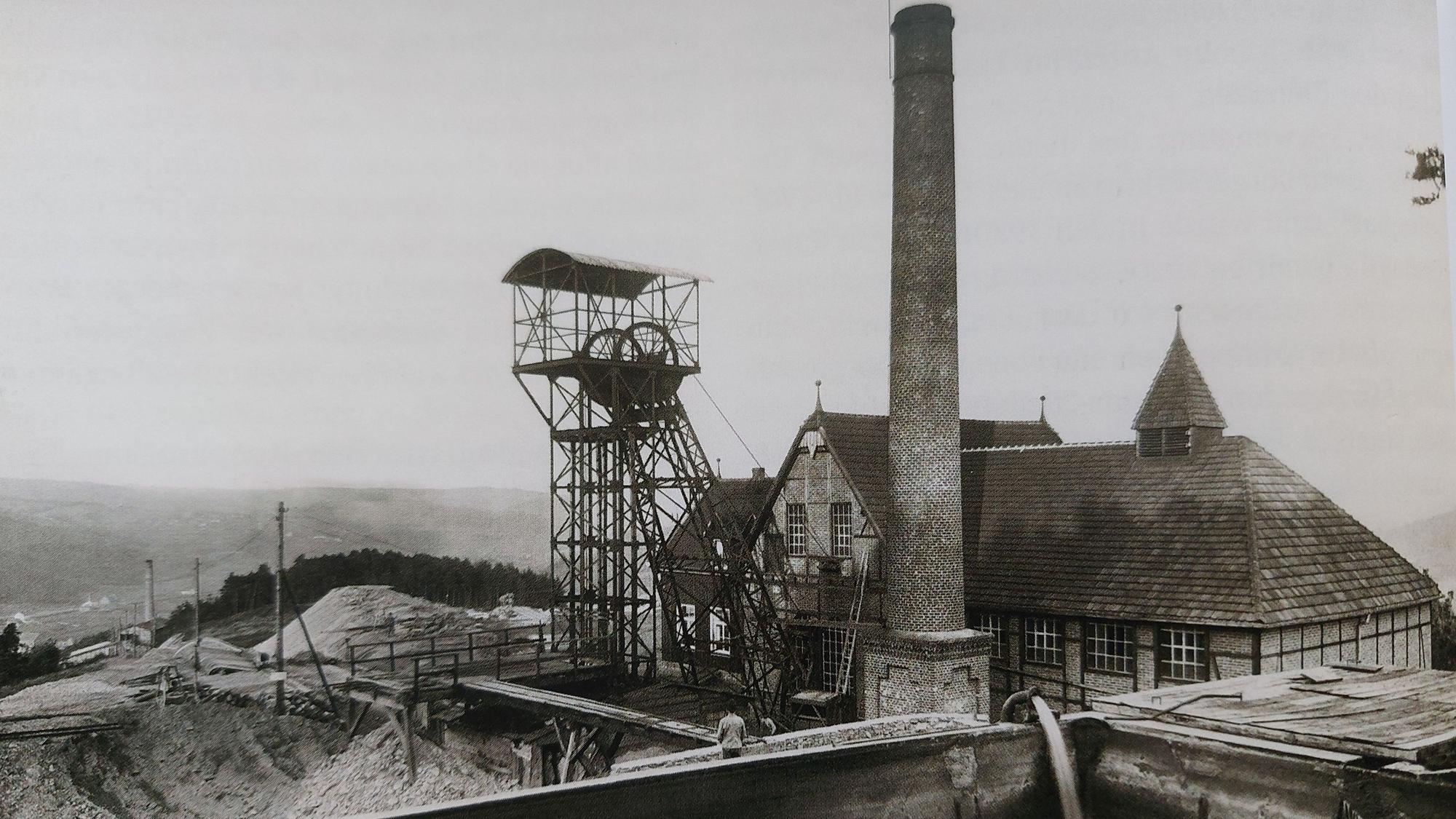 Historische Aufnahme einer alten Grubenanlage mit Förderturm und Schornstein, davor Halden.