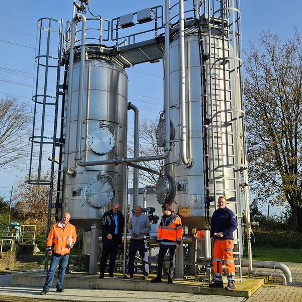 Fünf Männer stehen vor einer Anlage mit zwei silbern glänzenden Silos.