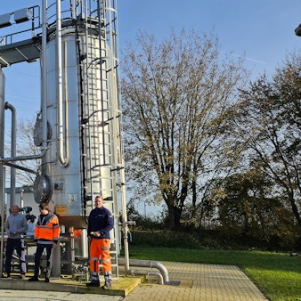 Fünf Männer stehen vor einer Anlage mit zwei silbern glänzenden Silos.