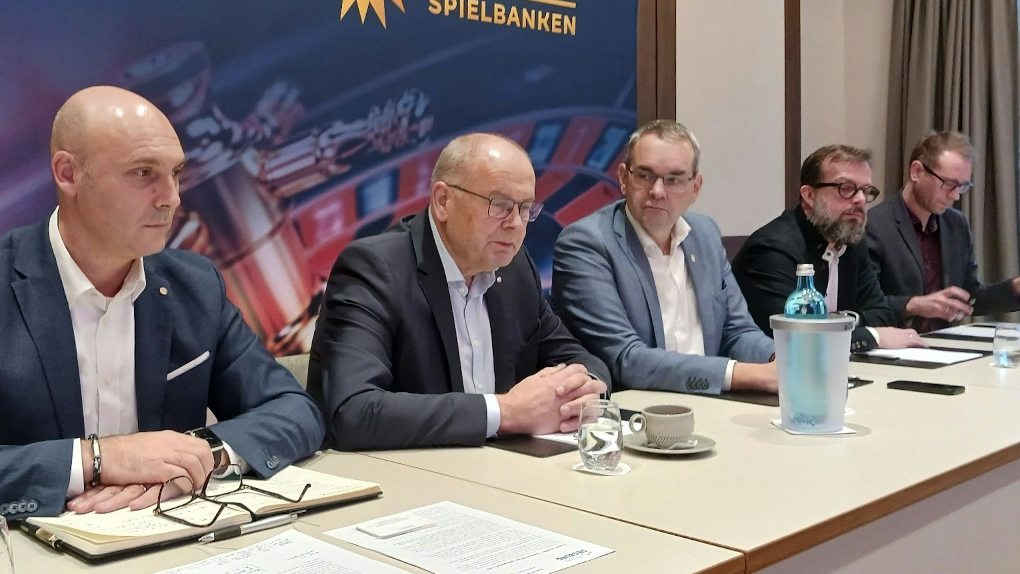 Fünf Männer sitzen bei einer Pressekonferenz an einem langen Tisch