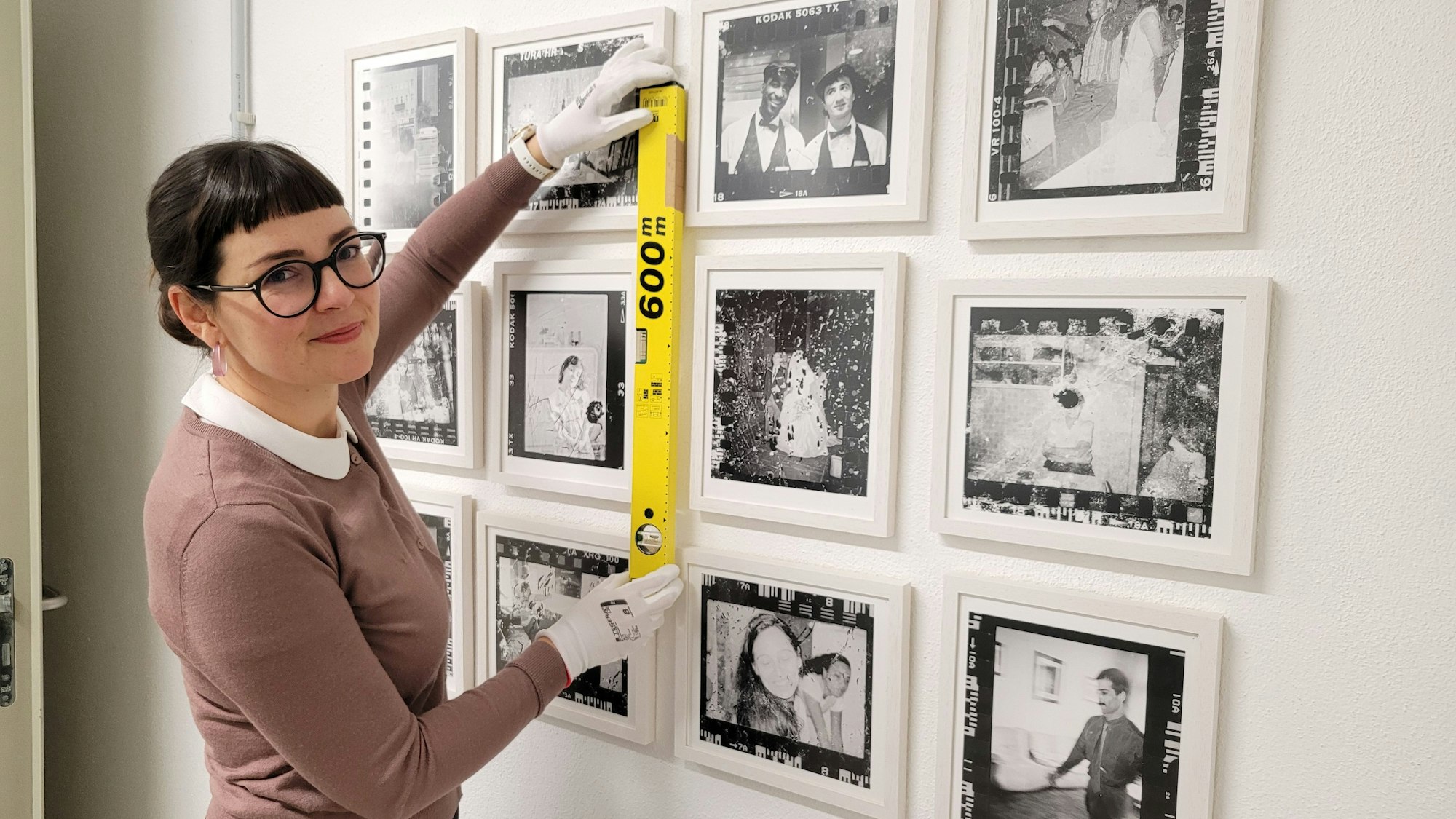 Eine dunkelhaarige Frau hängt Fotos für eine Ausstellung auf.