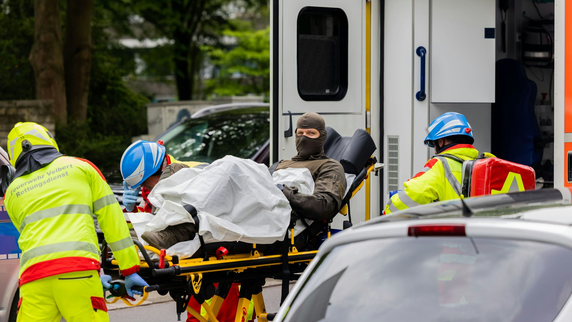 ARCHIV - 11.05.2023, Nordrhein-Westfalen, Ratingen: Ein verletzter Polizeibeamter wird vor einem Hochhaus in einen Krankenwagen gebracht.