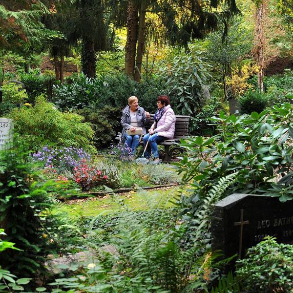 Zwei Frauen sitzen auf einem Friedhof auf einer Bank.