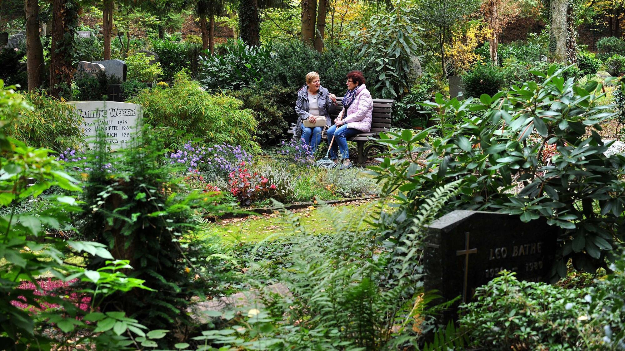 Zwei Frauen sitzen auf einem Friedhof auf einer Bank.