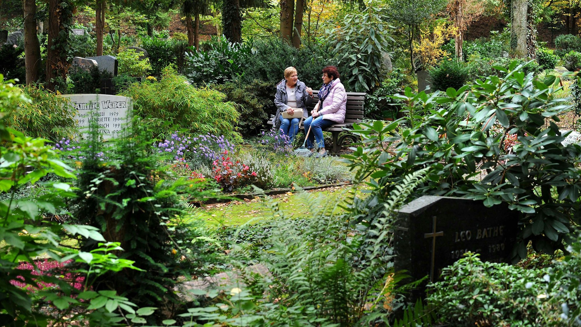 Zwei Frauen sitzen auf einem Friedhof auf einer Bank.