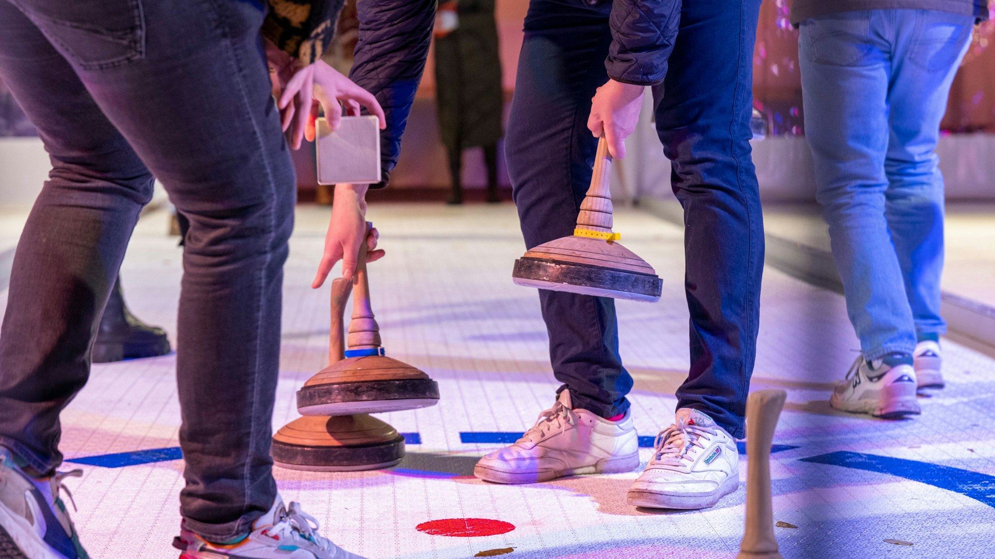 Zu sehen sind Menschen, die mit Eisstockschießen beschäftigt sind.