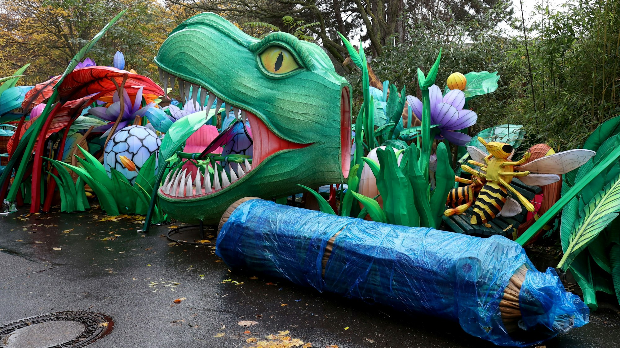 An einem Weg auf dem Hinterhof des Kölner Zoos türmen sich Einzelteile der Lichtskulpturen, darunter ein Dinosaurierkopf, Insekten und Pflanzen.