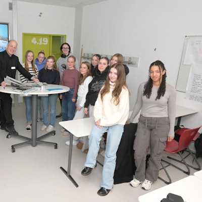 Schüler stehen mit Zeitungen in der Hand um einen Tisch.