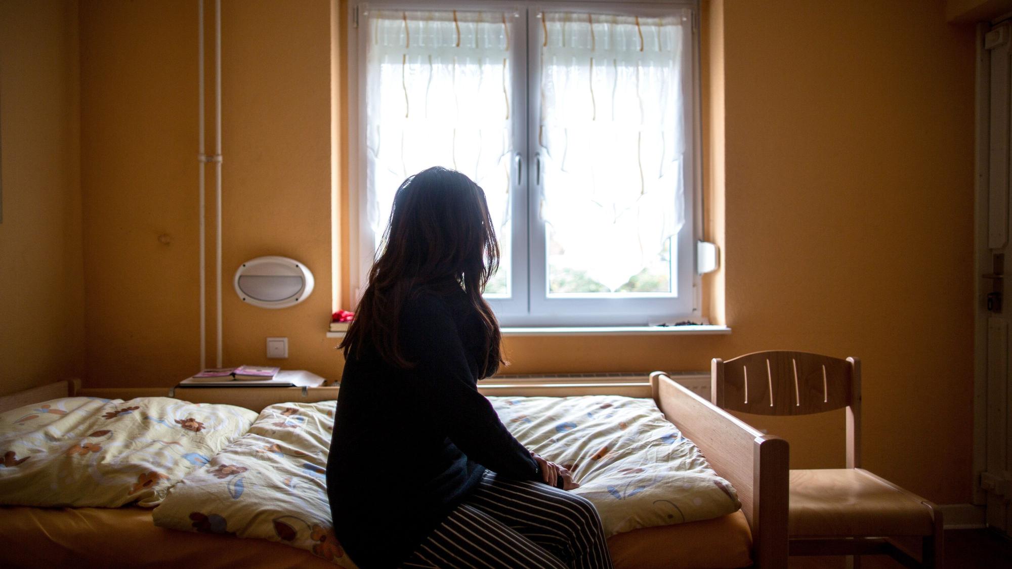 Eine Frau sitzt in einem Frauenhaus auf einem Bett.
