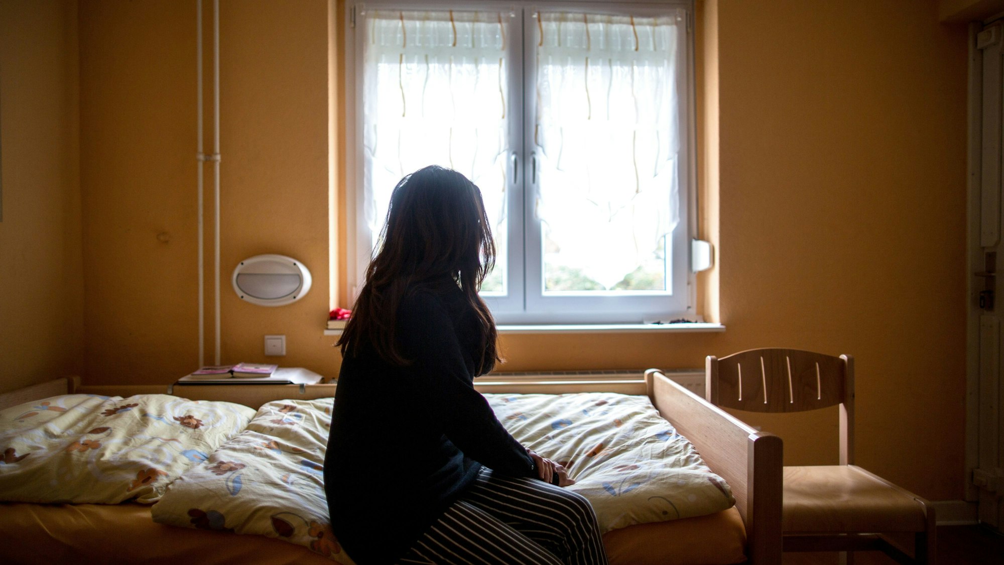 Eine Frau sitzt in einem Frauenhaus auf einem Bett.