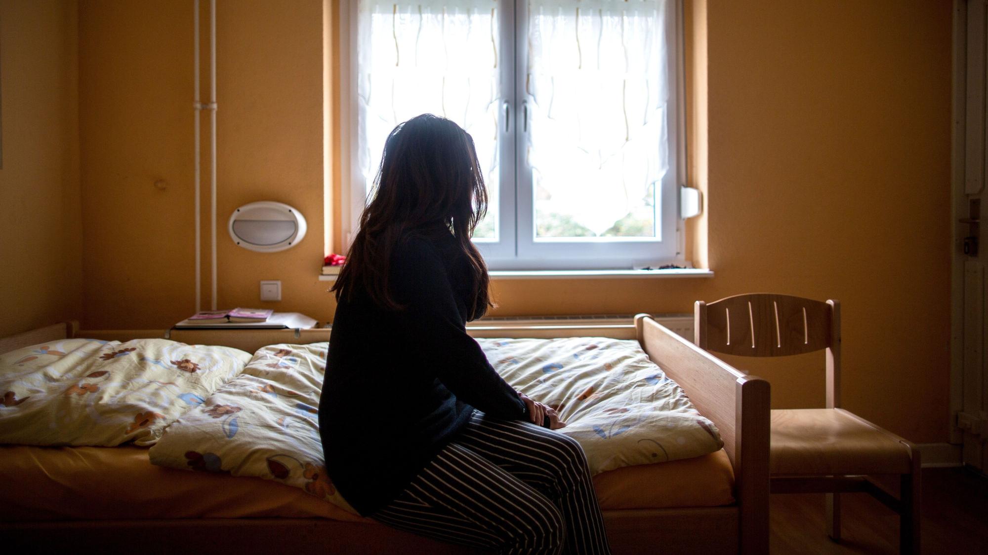 Eine Frau sitzt in einem Frauenhaus auf einem Bett.