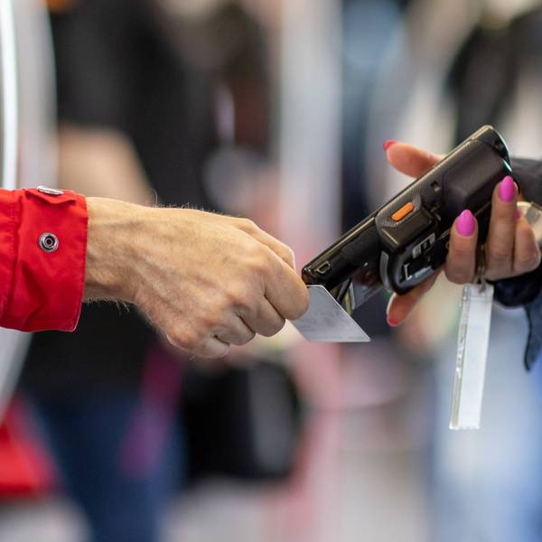 Zu sehen ist eine Fahrkartenkontrolleurin, die mit einem elektronischen Lesegerät in einer U-Bahn den Fahrschein eines Fahrgastes kontrolliert.
