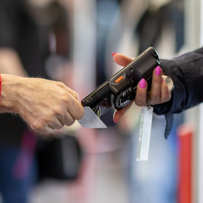 Zu sehen ist eine Fahrkartenkontrolleurin, die mit einem elektronischen Lesegerät in einer U-Bahn den Fahrschein eines Fahrgastes kontrolliert.