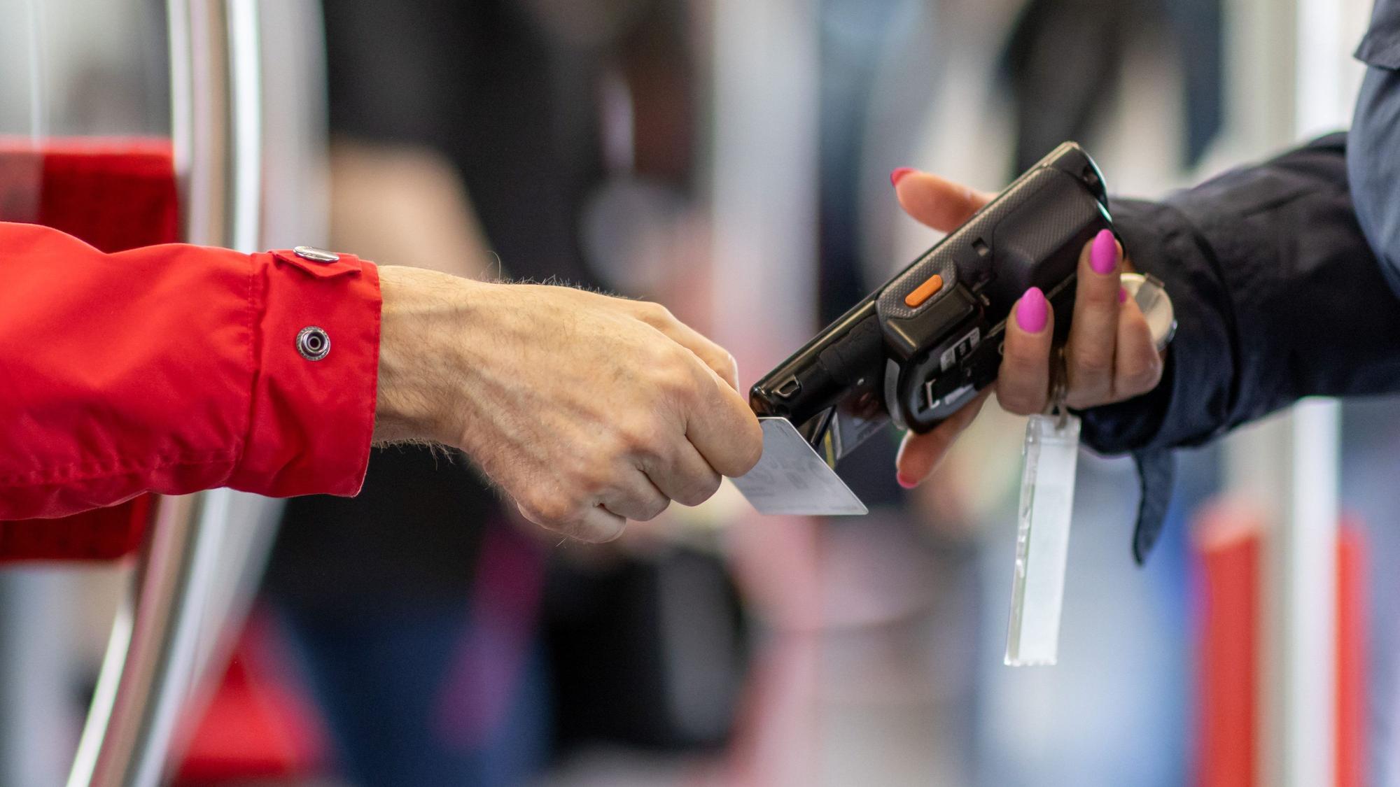 Eine Fahrkartenkontrolleurin kontrolliert mit einem elektronischen Lesegerät in einer U-Bahn den Fahrschein eines Fahrgastes