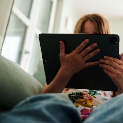 Ein Mädchen sitzt auf der Couch und schaut in das Tablet ihrer Eltern. (gestellte Szene) . (zu dpa: «Vorstellung einer Studie zu Einsamkeit unter Jugendlichen») Foto: Annette Riedl/dpa +++ dpa-Bildfunk +++