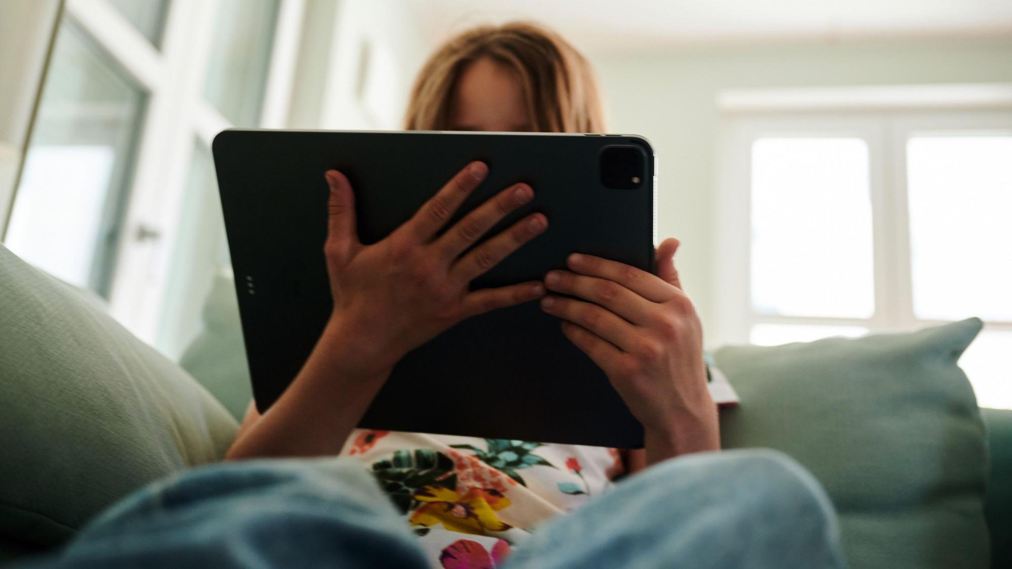 Ein Mädchen sitzt auf der Couch und schaut in das Tablet ihrer Eltern. (gestellte Szene) . (zu dpa: «Vorstellung einer Studie zu Einsamkeit unter Jugendlichen») Foto: Annette Riedl/dpa +++ dpa-Bildfunk +++
