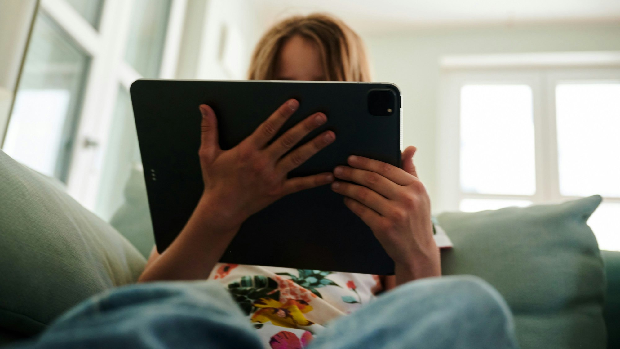Ein Mädchen sitzt auf der Couch und schaut in das Tablet ihrer Eltern. (gestellte Szene) . (zu dpa: «Vorstellung einer Studie zu Einsamkeit unter Jugendlichen») Foto: Annette Riedl/dpa +++ dpa-Bildfunk +++