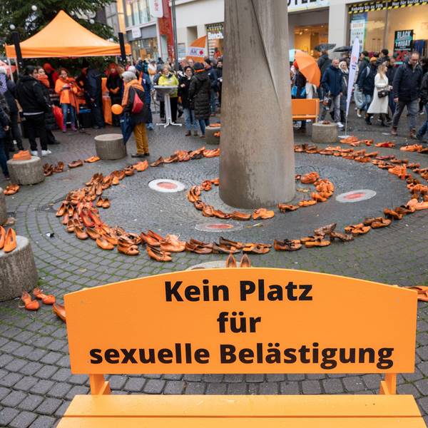 Orange Bank mit der Aufschrift „Kein Platz für sexuelle Belästigung“, im Hintergrund sind orange Schuhpaare kreisförmig aufgestellt