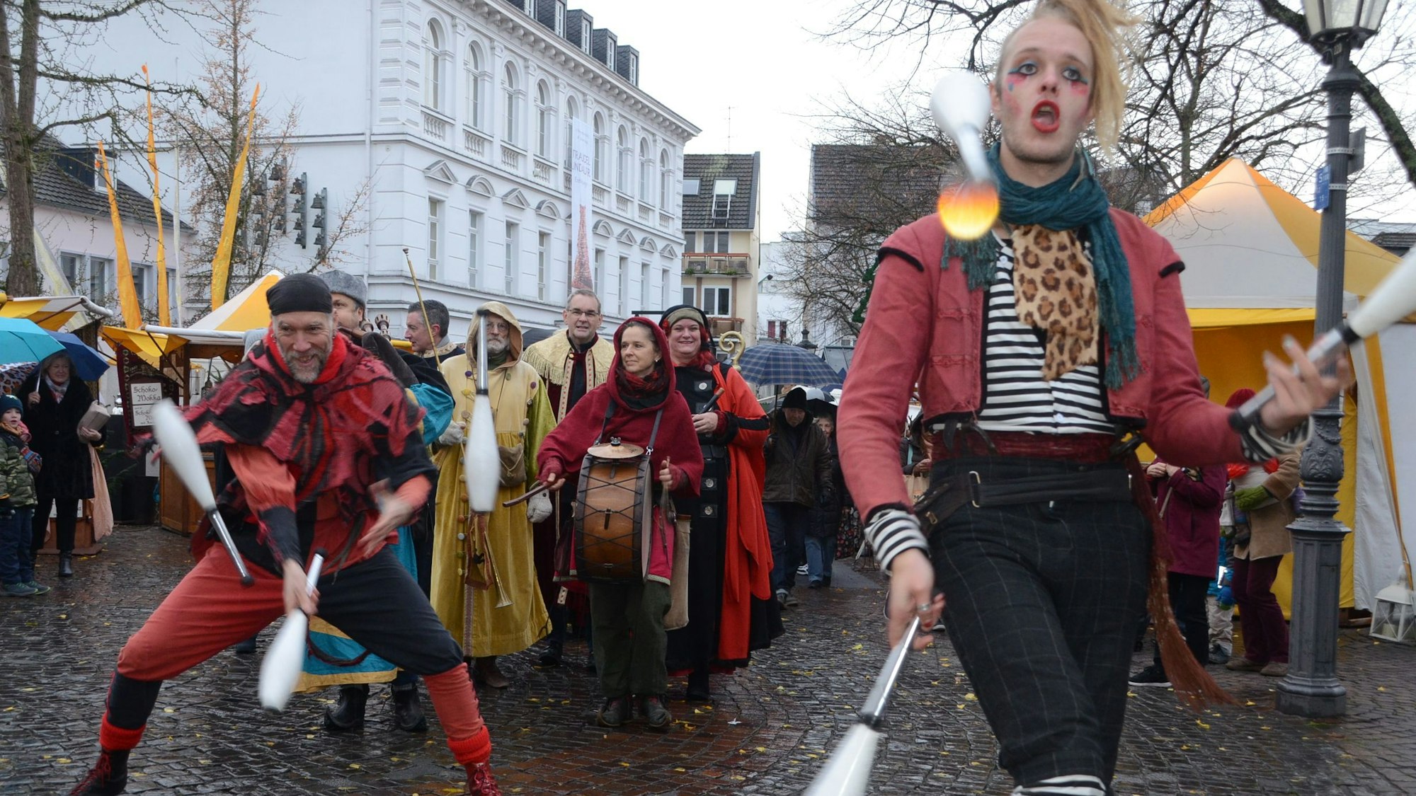 Gaukler in mittelalterlicher Kleidung schwingen Kegel durch die Lüfte und ziehen in einer Parade durch die Stadt.