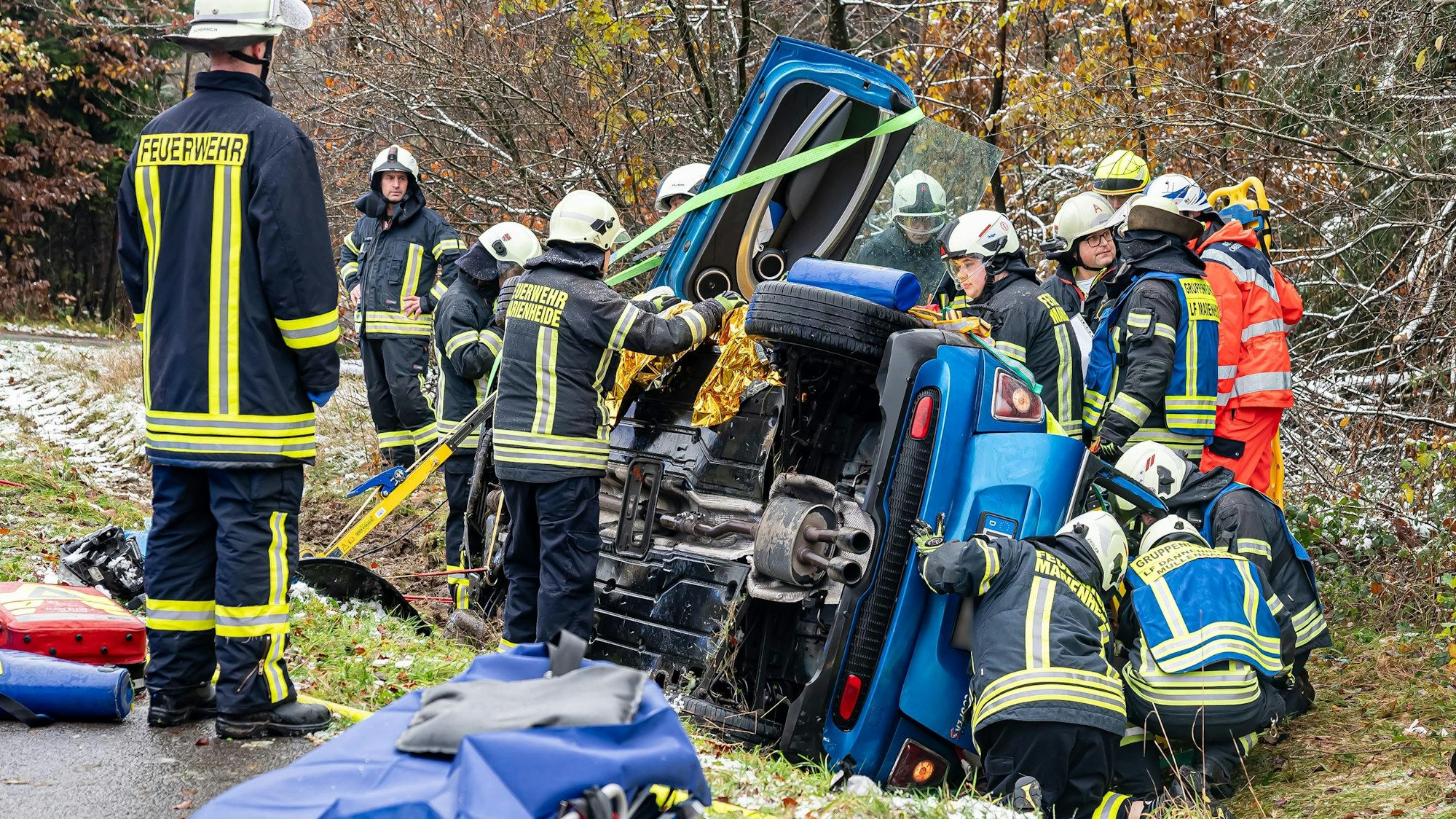 Mehrere Feuerwehrleute arbeiten an einem auf der Seite liegenden Auto.
