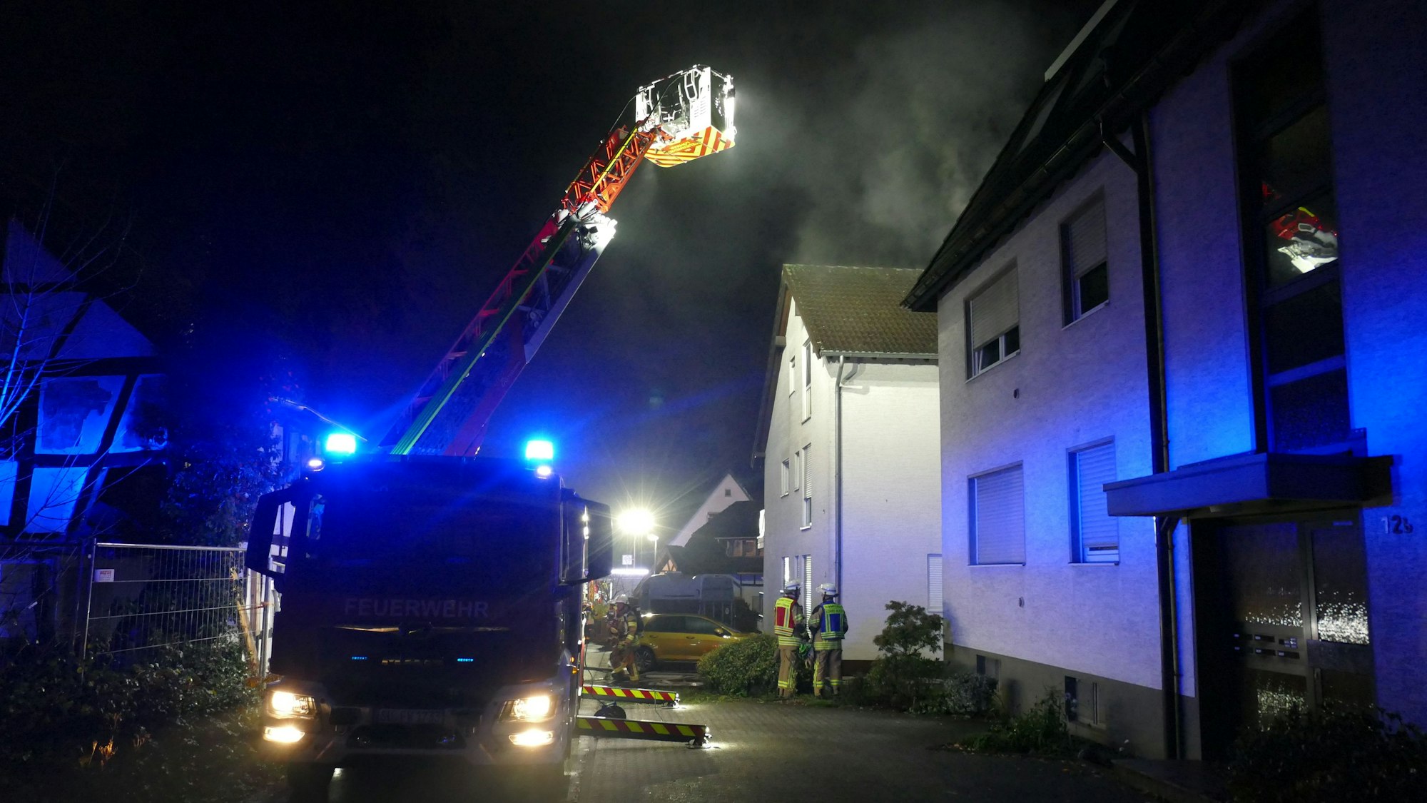 Eine Drehleiter der Feuerwehr steht in einer Gasse vor einem brennenden Haus.