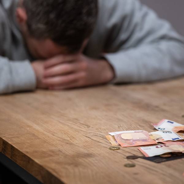Ein Mann hat seinen Kopf auf seine Hände gelegt, während sich vor ihm Geldscheine, Münzen und Bankkarten auf einem Tisch befinden.