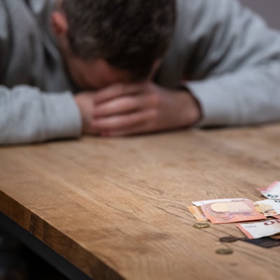 Ein Mann hat seinen Kopf auf seine Hände gelegt, während sich vor ihm Geldscheine, Münzen und Bankkarten auf einem Tisch befinden.